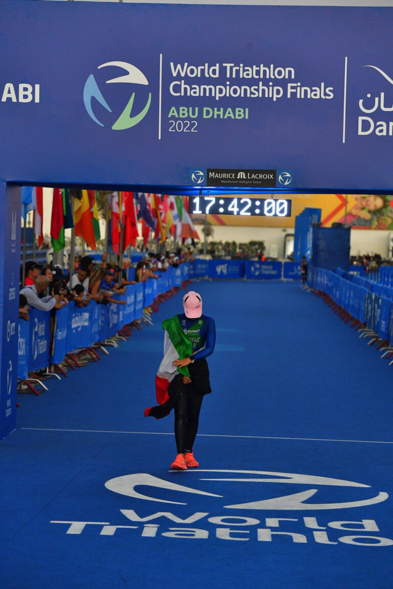 Lulwa Alrifaie crossing the finish line with the Kuwait flag at the World Triathlon Championship Finals in Abu Dhabi