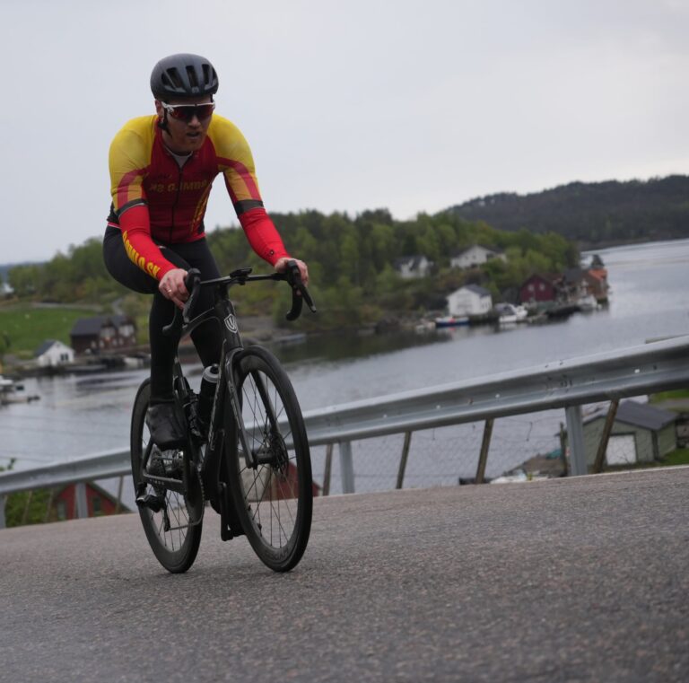 Svein Tore Bø racing his road bike along a waterside road in a red and yellow kit
